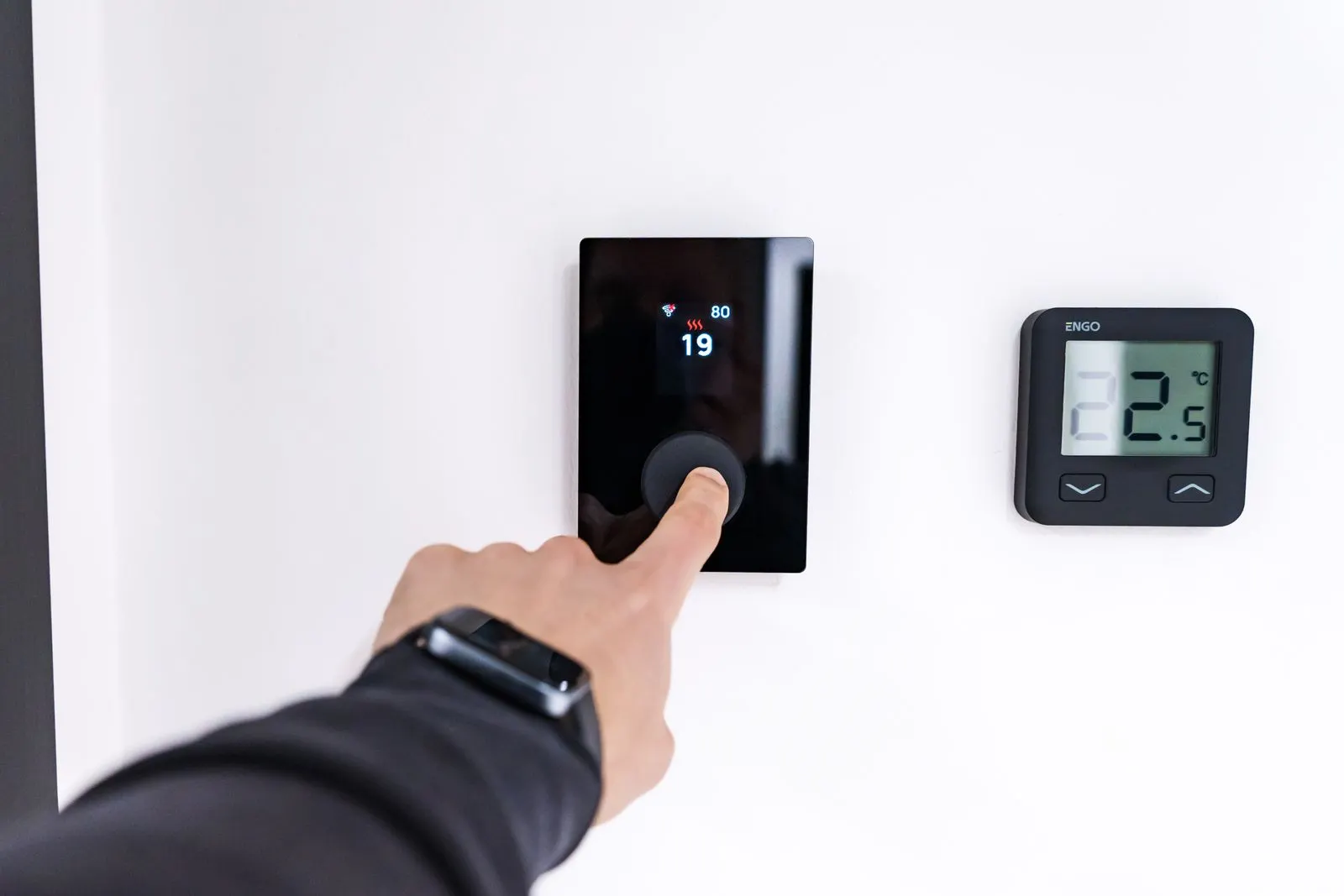 Hand adjusting a wall-mounted smart thermostat