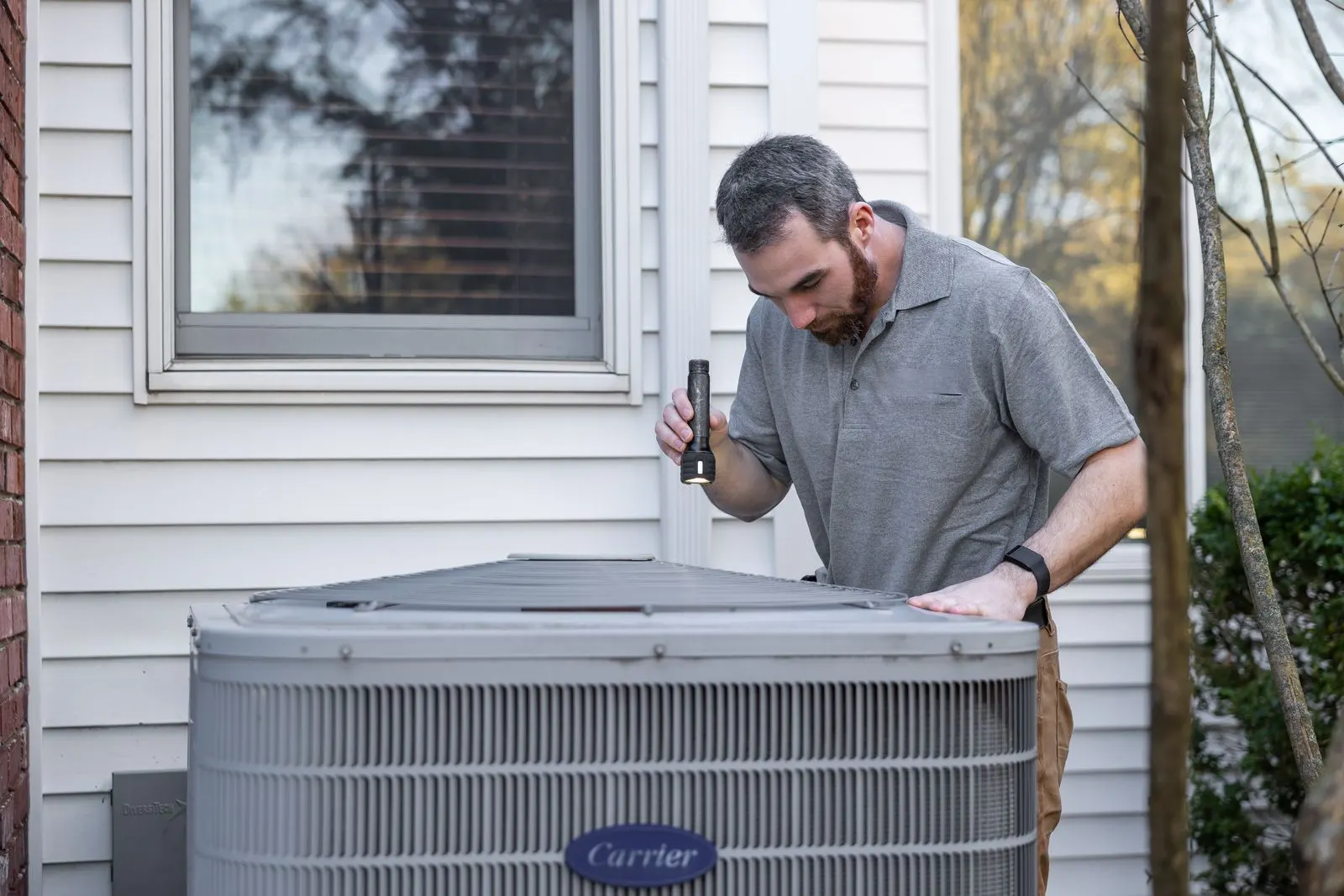 HVAC technician inspecting a central air conditioner outside a house